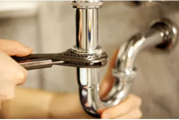 Hand mit Rohrzange am verchromten Siphon eines Waschbeckens